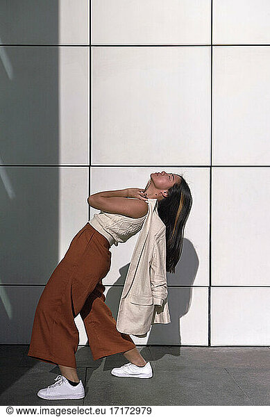 Young woman bending backwards by wall during sunny day