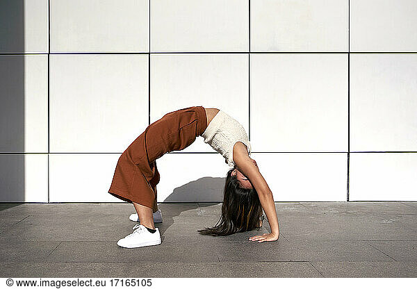 Young woman bending over backwards against wall during sunny day