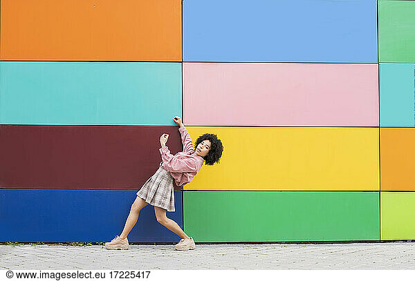 Young woman bending over backwards while standing by multi colored wall