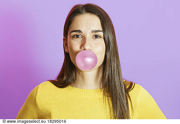 Young woman blowing bubble gum against purple background