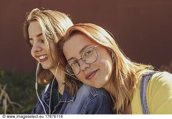 Young woman by friend listening music through in-ear headphones