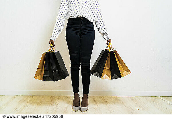 Young woman carrying paper shopping bags while standing against white background