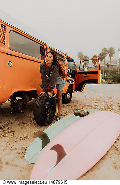 Young woman changing recreational vehicle tyre at beach  Jalama  California  USA