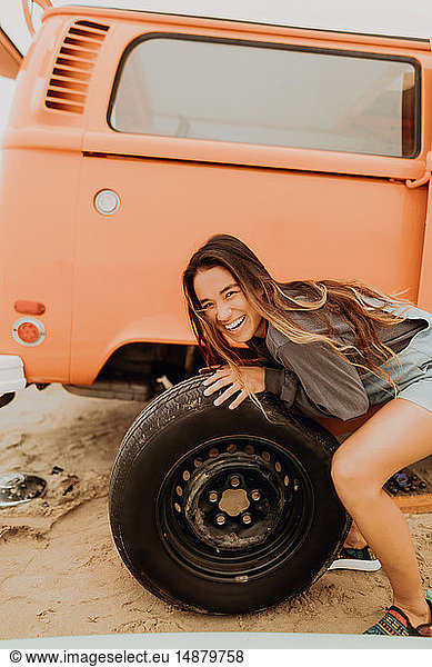 Young woman changing recreational vehicle tyre at beach  portrait  Jalama  California  USA