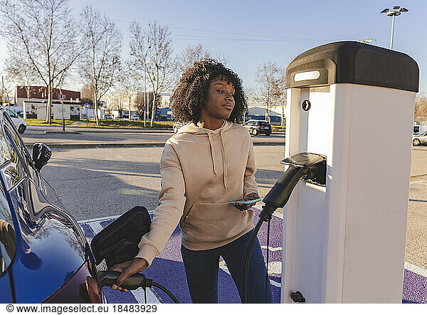 Young woman charging electric car at station