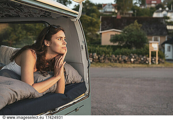 Young woman contemplating while lying down in van during road trip