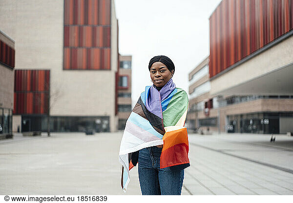 Young woman covered in mrainbow flag standing outside building