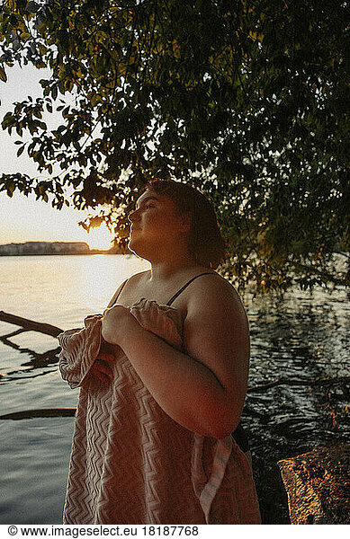 Young woman covering body with towel while looking away during sunset
