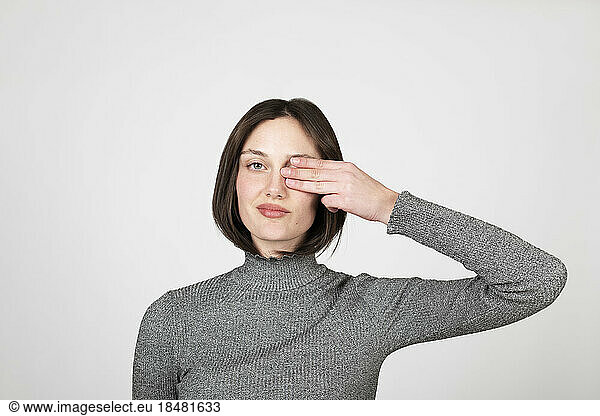 Young woman covering eye against white background