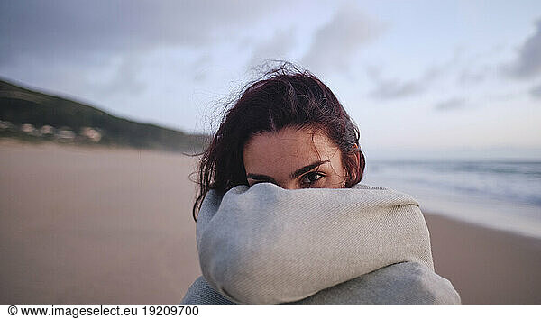 Young woman covering face with blanket at beach