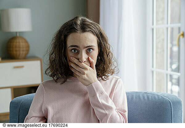 Young woman covering mouth with hand at home