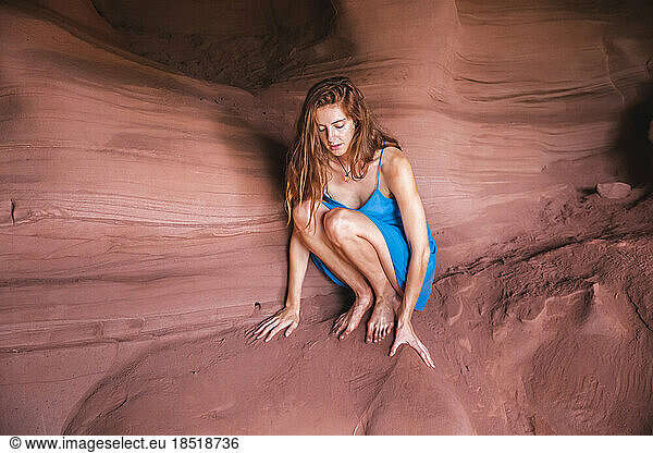 Young woman crouching on red rock in cave
