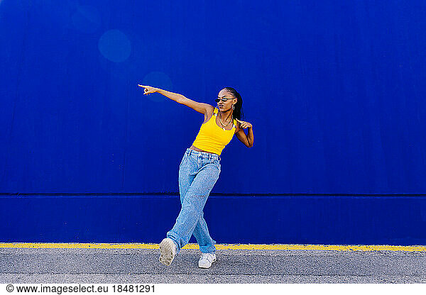 Young woman dancing in front of blue wall