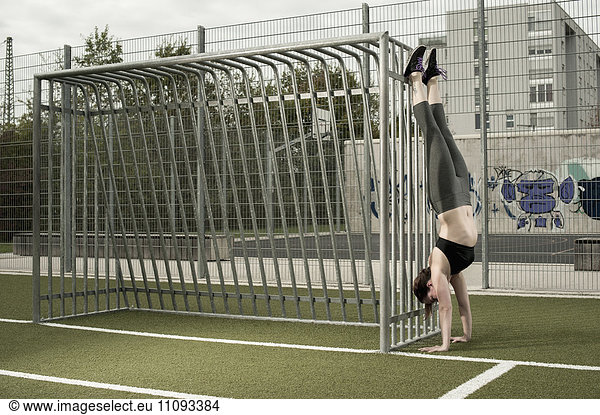 Young woman doing handstand on football ground