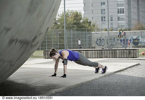 Young woman doing push-ups on floor and listening to music  Bavaria  Germany