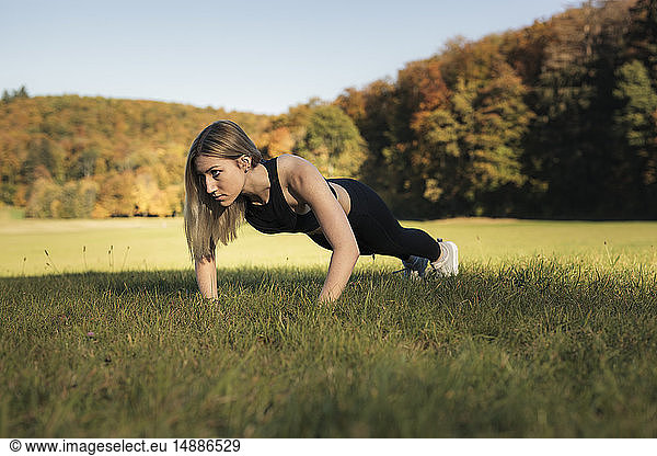 Young woman doing pushups during workout on meadow