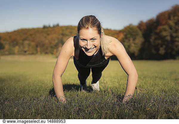Young woman doing pushups during workout on meadow