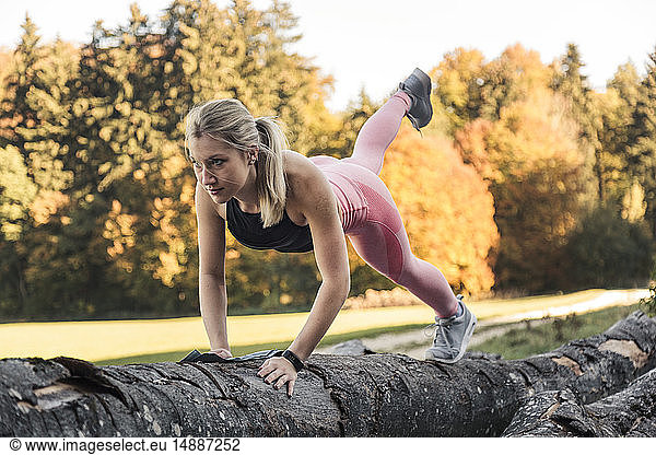 Young woman doing pushups on tree trunk during workout in nature