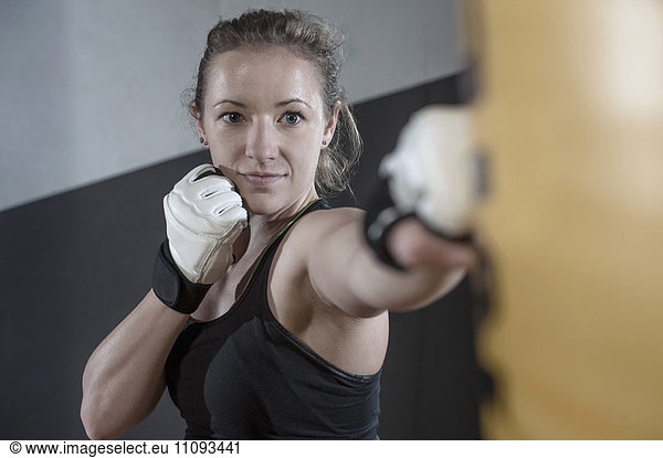 Young woman doing strength training by punching on punch bag in the gym