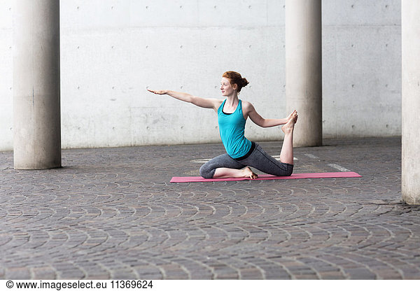 Young woman doing yoga on exercise mat in urban city