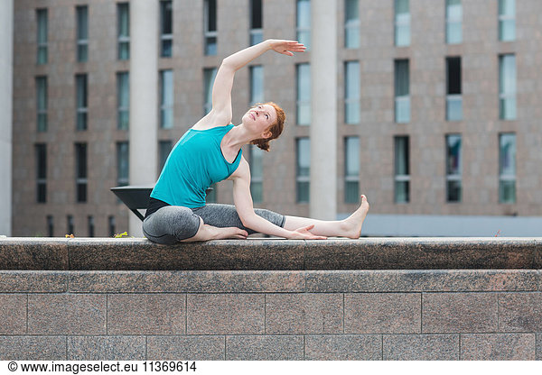 Young woman doing yoga on wall in urban city