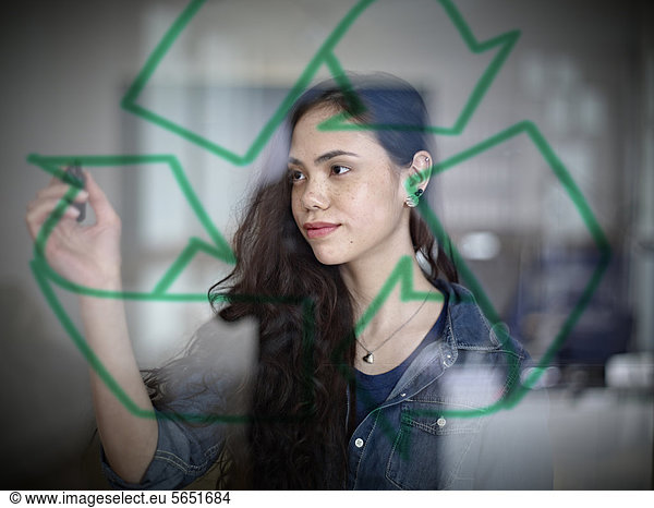 Young woman drawing recycling symbol on glass