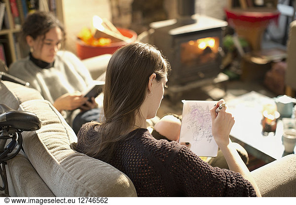 Young woman drawing  sketching in notepad in living room