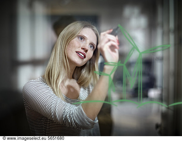 Young woman drawing wind turbine on glass