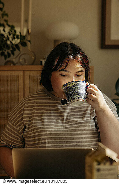 Young woman drinking coffee while using laptop at home