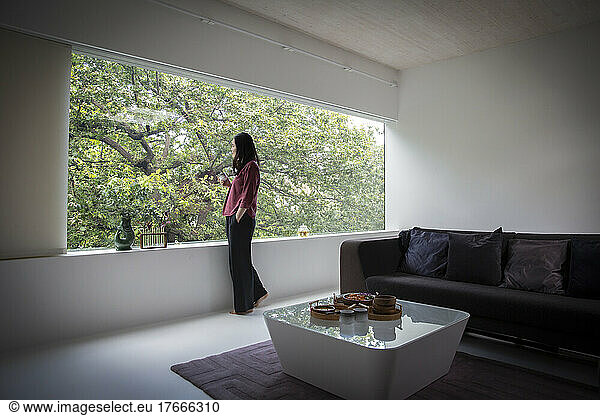 Young woman drinking tea at window in modern living room