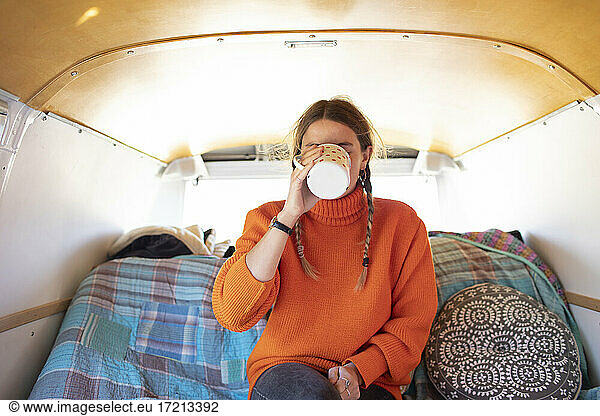 Young woman drinking tea in camper van