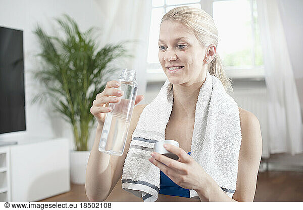 Young woman drinking water after exercise at living room and smiling  Bavaria  Germany