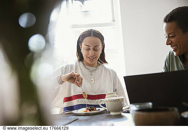 Young woman drizzling honey over breakfast at dining table