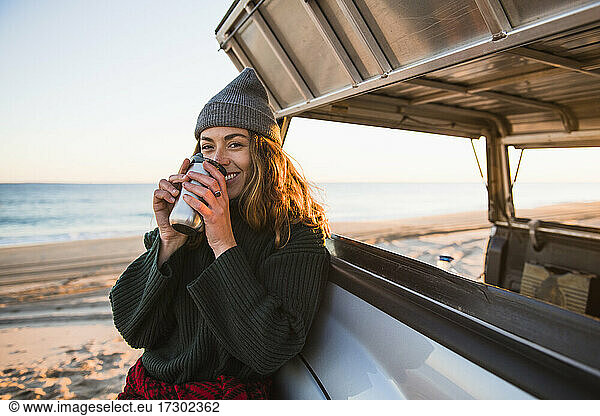 Young woman enjoying coffee in travel mug while beach car camping