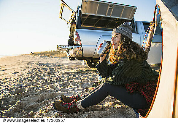 Young woman enjoying coffee in travel mug while beach car camping
