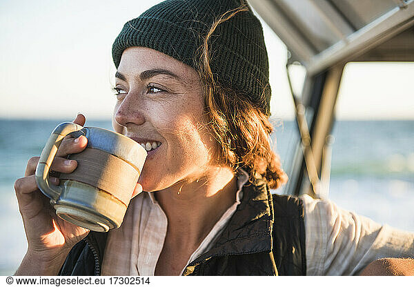 Young woman enjoying drink in mug while beach car camping alone