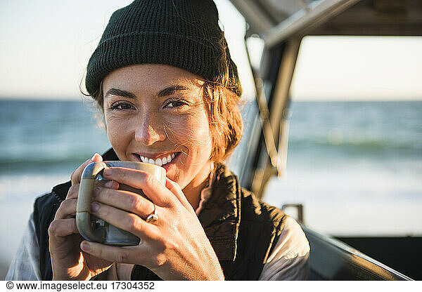 Young woman enjoying drink in mug while beach car camping alone