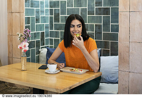 Young woman enjoying snacks with coffee in cafe