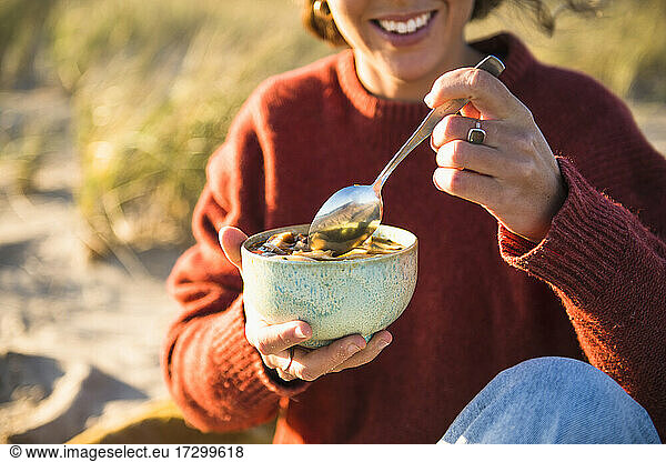 Young woman enjoying soup while beach car camping alone