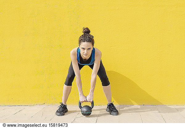Young woman exercising with dumbbell in front of a yellow wall