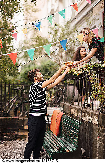 Young woman giving food to smiling male friend from balcony during garden party
