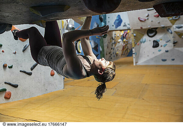 Young woman hanging upside-down from rock wall
