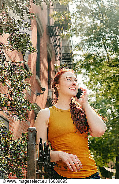 Young woman happily talking on phone outdoors in Brooklyn street.