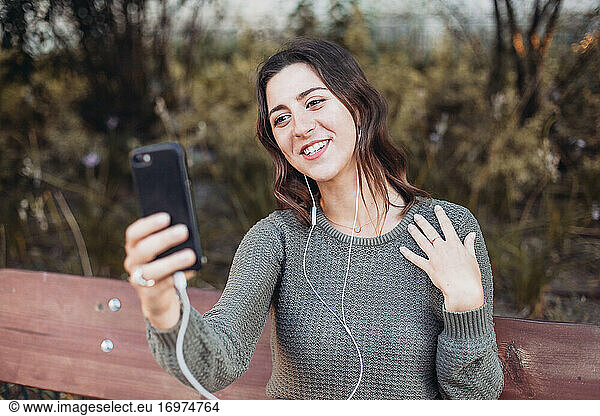 Young woman having a video call  on a bench outdoors