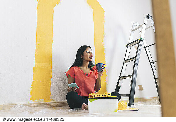 Young woman having coffee while holding mobile phone in living room