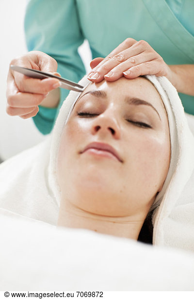 Young woman having eyebrows plucked from tweezers at beauty spa