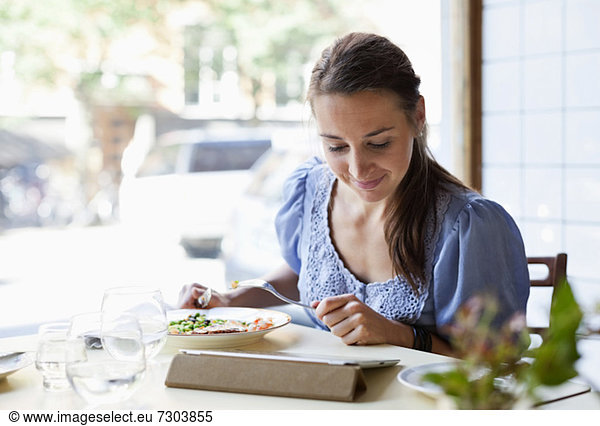 Young woman having meal while using digital tablet at restaurant table