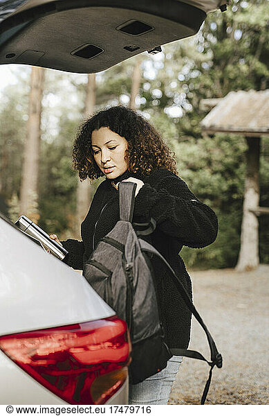 Young woman holding backpack by car during vacation