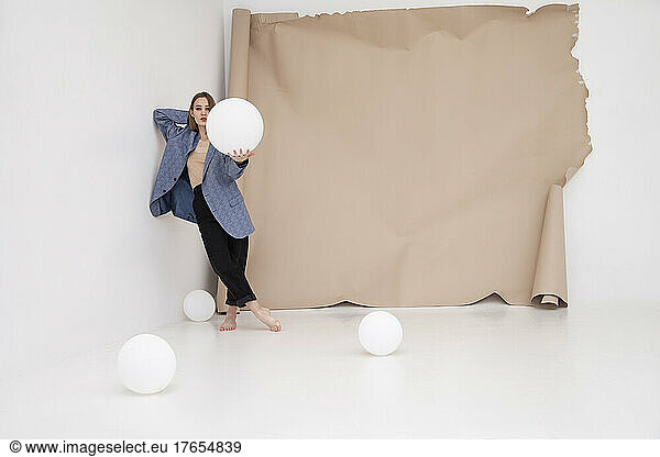 Young woman holding balloon standing against brown backdrop
