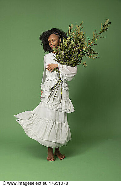 Young woman holding bunch of leaves standing against green background
